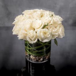 Compact arrangement of white roses in a clear glass cylinder vase with stones at the base