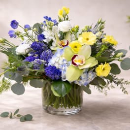 Mixed bouquet of yellow, blue, and white flowers in a glass vase