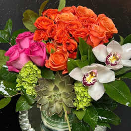 Bouquet of orange and pink roses with white orchids in a glass vase