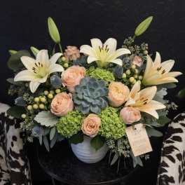 Peach roses and white lilies arranged in a white vase with a succulent centerpiece