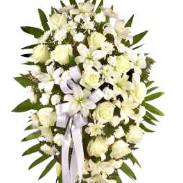 White floral standing spray with roses and lilies, accented by a pale ribbon
