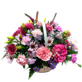 Basket arrangement of pink carnations, roses, and purple daisies with mixed pastel flowers.