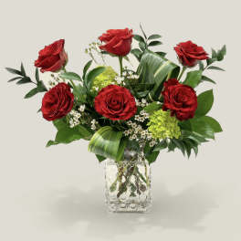 Red roses arranged in a clear square vase with mixed greenery