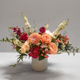 Mixed bouquet of roses, chrysanthemums, and white spikes in a cream vase