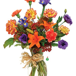 Bright mixed bouquet of orange lilies, purple irises, and assorted blooms in a clear glass vase