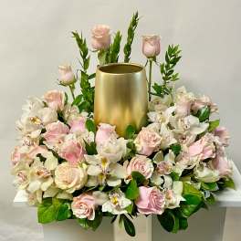 Pink roses and white orchids arranged around a gold cylinder vase
