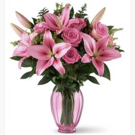 Pink lilies and roses arranged in a pink glass vase