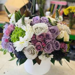 Lavender and white roses arranged in a white vase with white daisies