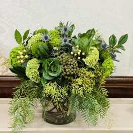 Green floral arrangement in a glass vase with trailing foliage
