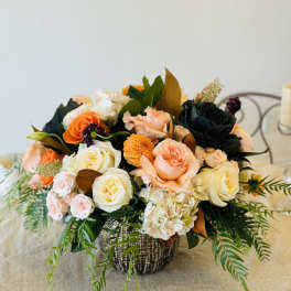 Mixed bouquet of peach, white, and orange roses in a woven basket