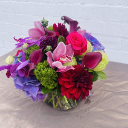 Bright mixed bouquet with pink roses, purple orchids, and burgundy calla lilies in a glass vase