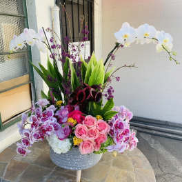 Large floral arrangement with pink roses, orchids, and white orchids in a gray vase