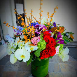Large mixed floral arrangement in a green vase with orchids and roses