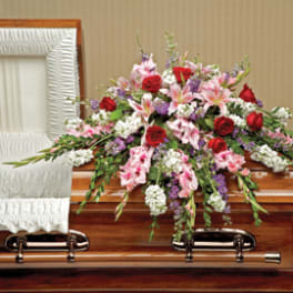 Casket spray of red roses, pink lilies, and mixed blooms arranged on a wooden casket