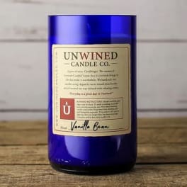 Blue glass jar candle with cream label reading Unwined Candle Co. Vanilla Bean on wooden surface