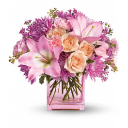 Pink lilies, peach roses, and lavender flowers arranged in a pink glass cube vase