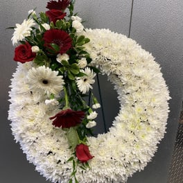 Circular white floral wreath with red roses and burgundy daisies