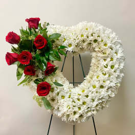 Heart-shaped floral wreath with white daisies and red roses on a stand
