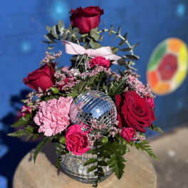 Pink and red roses arranged around a mirrored disco ball in a glass vase