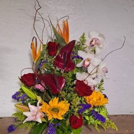 Tropical floral arrangement with roses, orchids, and sunflowers in a white container