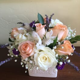 Arrangement of peach and white roses with purple accents in a ceramic vase