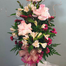 Tall pink and white rose and alstroemeria arrangement in a dark glass vase with glittery ribbons