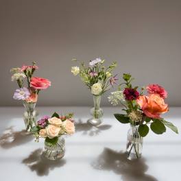 Set of small mixed flower arrangements in clear ribbed glass vases on a light surface