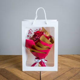Bouquet of red roses in pink and gold wrap inside a white gift bag