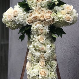 White floral cross with cream roses and hydrangeas on a stand