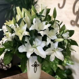 White lilies arranged in a white vase with a cross emblem