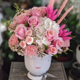 Pink roses and white hydrangeas in a white face vase with pink feathers