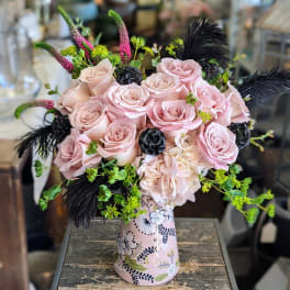 Pink roses and pale hydrangea in a floral vase with black feathers