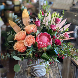 Peach roses and pink protea in a striped ceramic vase