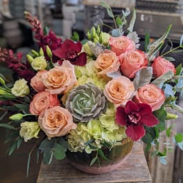 Peach and pink roses with burgundy orchids in a low bowl arrangement