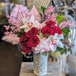Bouquet of red roses and white orchids in a printed vase with pink feathers