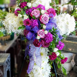 Cross-shaped floral spray with white chrysanthemums, pink roses, and purple ribbon