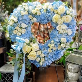 Heart-shaped wreath of blue hydrangeas and white roses on a stand