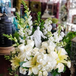 White floral arrangement with roses, lilies, and a small statue centerpiece