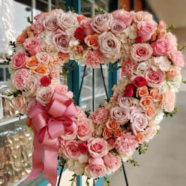 Heart-shaped pink and peach rose arrangement with a satin bow
