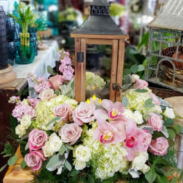 Pink roses and orchids arranged around a wooden lantern centerpiece