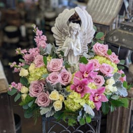 Pink roses and orchids arranged around a white angel statue