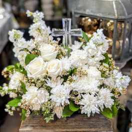 White floral arrangement with roses, daisies, and a clear glass cross
