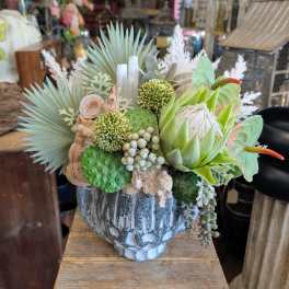 Succulent arrangement in a weathered gray vase with pale green and white accents.