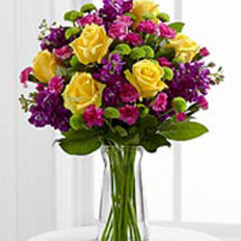 Bouquet of yellow roses and purple flowers in a clear glass vase
