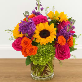 Bright bouquet of sunflowers, pink roses, and purple flowers in a glass vase