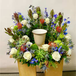 Large floral arrangement with white roses, blue flowers, and succulents in a cream urn