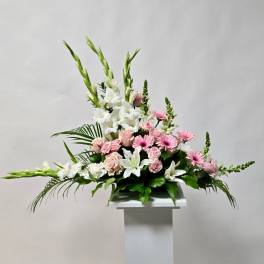 Pink and white floral arrangement with lilies, roses, and gerbera daisies on a pedestal
