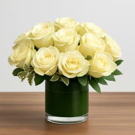 Short glass vase of pale yellow roses arranged in a tight, rounded cluster