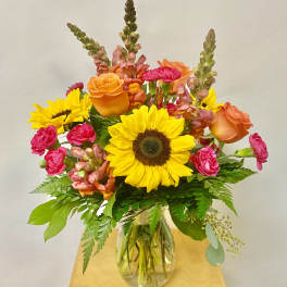 Bright mixed bouquet with sunflowers, orange roses, and pink blooms in a glass vase