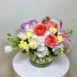 Mixed bouquet of roses, tulips, hydrangeas, and carnations in a glass vase